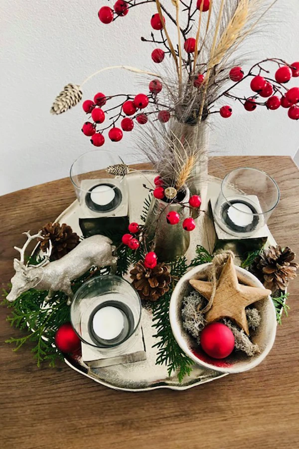 Weihnachtsarrangement mit Hagebutten in Vasen, silberner Hirschfigur und Kerzen
