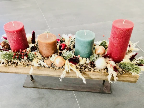 Weihnachtliches Gesteck auf Holz mit Christbaumkugeln und bunten Kerzen