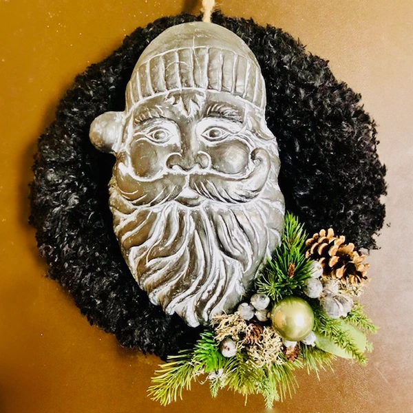 Schwarzer weihnachtlicher Dekokranz für die Wand mit einem Kopf des Weihnachtsmanns in der Mitte und Christbaumkugeln