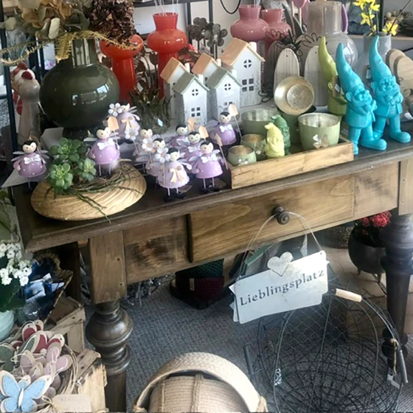 Dekotisch mit bunten Vasen, kleinen Häuschen, Figuren, Pflanzen und weiteren Wohnaccessoires.