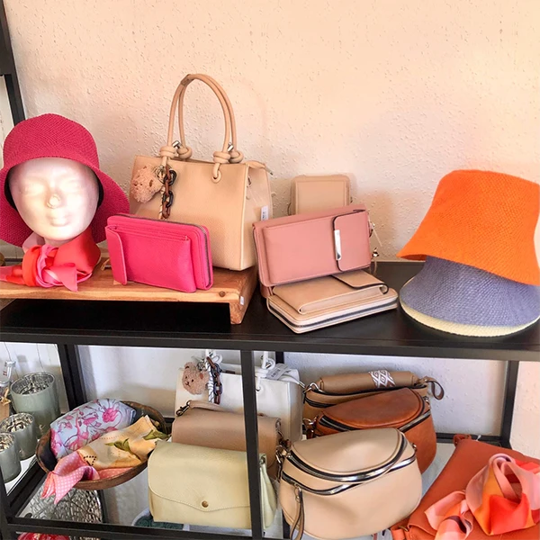 Regal mit Damenhüten, Handtaschen, Portemonnaies und Tüchern in Rosa-, Beige- und Orangetönen.