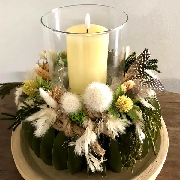 Dekoratives Kerzenarrangement mit Trockenblumen, Federn und grünen Blättern