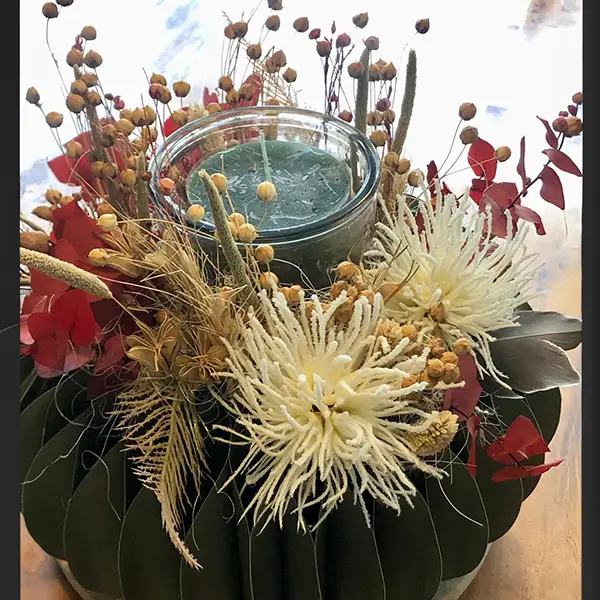 Herbstliches Gesteck mit Kerze, Trockenblumen und roten Blättern