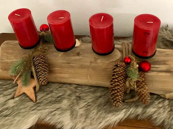 Rustikaler Adventskranz auf Holzbrett mit vier roten Kerzen und Tannenzapfen